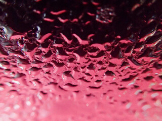 Water liquid droplets pattern on a metal surface with red and black reflection.