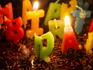 Close up of a happy birthday letter candles on a chocolate cake with chocolate rice topping.