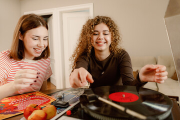 Two young women share joyful moments as they spin vinyl records in a cozy living room. Surrounded by colorful artwork and fresh fruit, they create lasting memories with laughter and music.