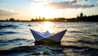 Paper boat sailing on water at sunset with city skyline.