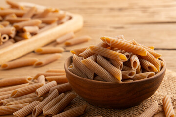 Organic whole wheat pasta,durum semolina flour macaroni,uncooked Penne rigate in wooden bowl.