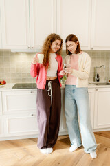 Two friends stand together in a modern kitchen, sipping drinks and sharing laughter. The warm sunlight fills the space, highlighting joyful moments and a sense of togetherness.