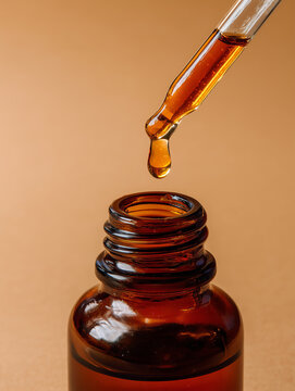 A single drop of amber liquid falling from a glass dropper into an open brown bottle, symbolizing natural skincare, beauty, and cosmetic product development