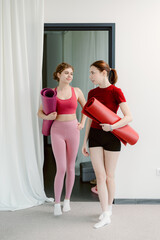 Obraz premium Two friends walk into a spacious yoga studio, each carrying a colorful yoga mat. They share smiles and excitement as they prepare for a rejuvenating session together.
