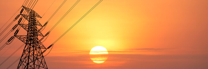 Power lines silhouetted against a vibrant sunset sky. The towering metal structure and electrical wires are set against a colorful backdrop