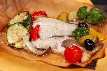 Sea bass fillet baked with zucchini, tomatoes, olives, and herbs served on a plate with parchment paper