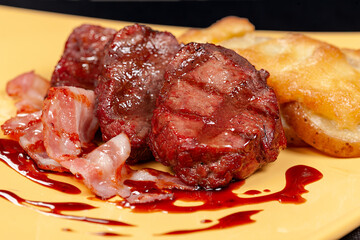 Grilled filet mignon with bacon and baked potato served with a red sauce on a yellow plate