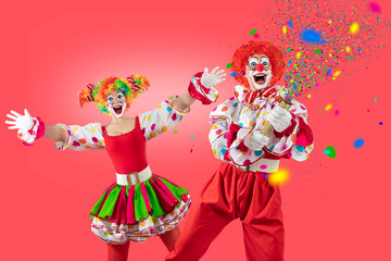 Funny male and female clowns celebrating and pointing upward on bright pink background. Cheerful circus concept with copy space for advertising and promotions.