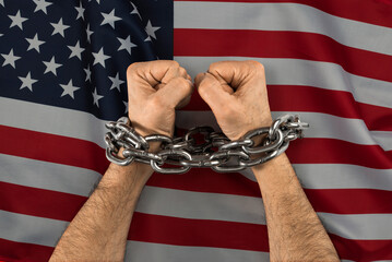 Men's hands chained against the USA flag