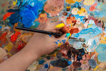 Artist's hands with old used brushes in an artist's studio, palette with multi-colored spots of oil or acrylic paint