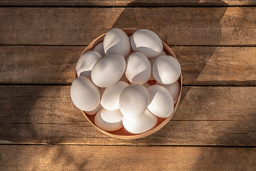 Chicken eggs in wooden bowl on grunge table in chicken coop, barn. Countryside outdoor setting in the backyard