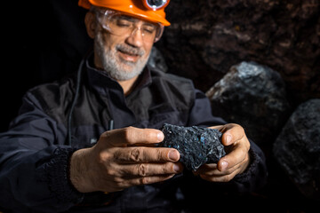 Hands of man in a hard hat with a flashlight examines rock, ore, rare earth metal. Geology, speleology, mining with a scientific approach