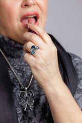 Close-up of a woman applying lipstick while wearing a gemstone ring and owl pendant.