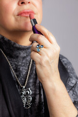 Close-up of a woman applying lipstick while wearing a gemstone ring and owl pendant.