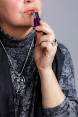 Close-up of a woman applying lipstick while wearing a gemstone ring and owl pendant.