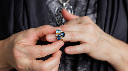 Close-up of hands displaying a blue gemstone ring against dark fabric.
