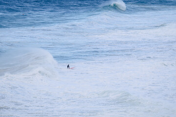 Fototapeta premium Surfer riding a massive ocean wave in a vast blue seascape at sea