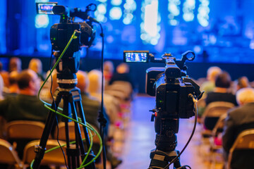 Professional video cameras positioned in a concert venue, capturing the performance with blurred audience in the background, showcasing the excitement of live events and cinematography