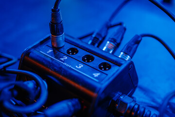 Audio interface with multiple input and output connections, surrounded by tangled cables, illuminated by blue lighting, showcasing the complexity of sound equipment and technology