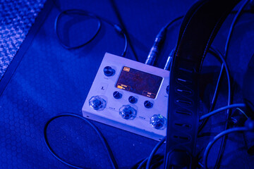 Electronic music effects pedal with illuminated display and knobs, surrounded by tangled cables on textured surface, creating a vibrant atmosphere for sound production
