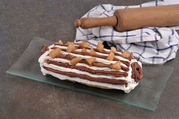 B&ucirc;che de No&euml;l poire et chocolat faite maison dans un plat avec un rouleau &agrave; p&acirc;tisserie et un torchon sur fond gris