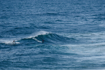 Obraz premium Surfers riding large ocean waves in a bright blue sea, capturing action and adventure