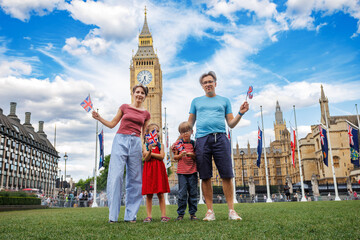 Family with flags pose in front of Big Ben on summer London trip