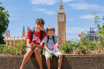 Two kids tourists with flags at Big Ben in a sunny London day