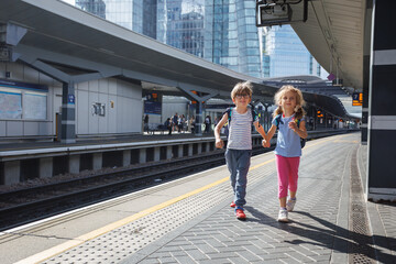 Happy kids commute with backpacks at the train station platform