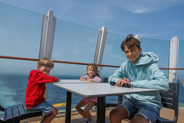 Three kids enjoy a sunny day on boat deck together, family trip