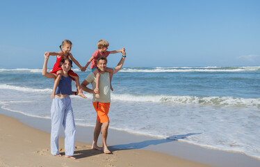 Parents and kids happily walk along sunny sandy beach in summer