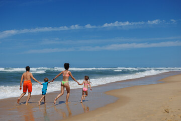 Family with two kids runs by waves, hold hands at summer beach