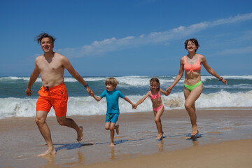 Smiling family of four races along the waves in bright swimwear