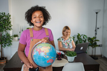 Smiling girl holding globe learning geography at home