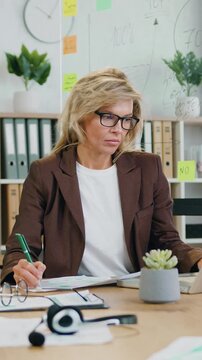 Woman head of company in eyeglasses and formal wear sitting at her workplace and previsioning financial documents and statistic on computer