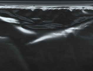 Wrinkled plastic wrap texture on a black background. Cellophane package wallpaper