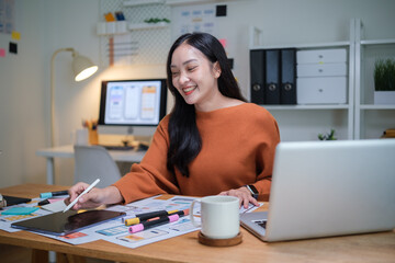 Smiling UX UI designer working with tablet and stylus on mobile app wireframes at desk.