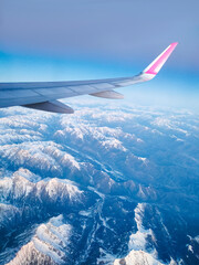 Aerial view of airplane wing flying over snow covered alps mountain range