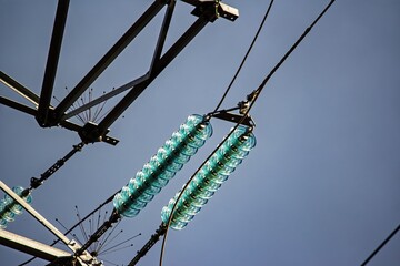 Close-up of sparkling glass disc insulators on a high-voltage power line against a clear blue sky,...