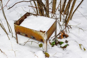 Rusty disposable grill, forgotten in fresh snow. Nature's quiet winter scene marred by human litter, a stark reminder of environmental impact