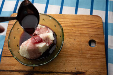 Traditional semolina pudding dessert with red wine sauce being poured