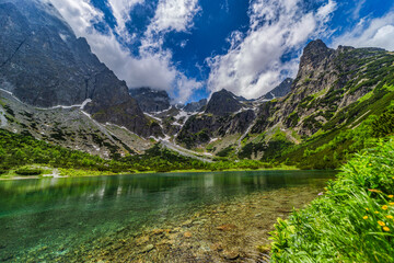 A stunning wide panorama of Zelene pleso (Green Lake) with the historic mountain hut and jagged...