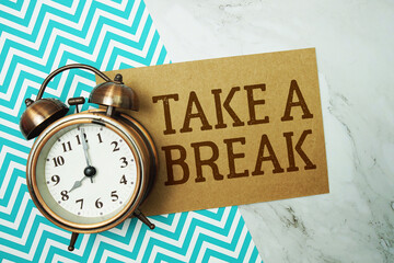Take A Break text written on paper card with alarm clock on marble background