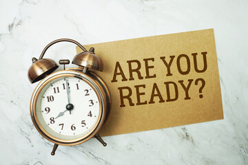 Are You Ready? text written on paper card with alarm clock on marble background