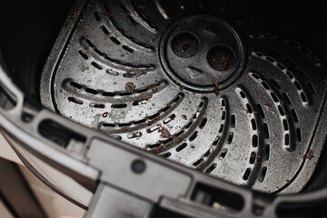 Dirty air fryer basket closeup. Burnt food residue on nonstick coating. Cleaning teflon surface detail. Kitchen appliance maintenance scene. Grease and crumbs after cooking. Household hygiene concept.