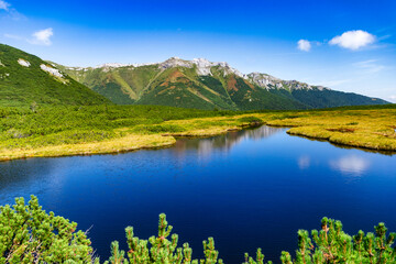 A peaceful view of Trojrohe pleso in the High Tatras. The crystal blue water reflects the sky,...