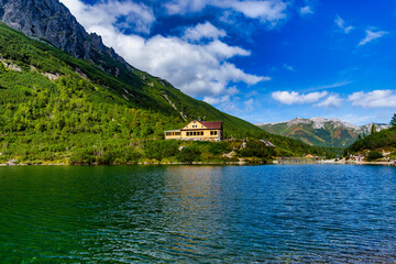 The famous wooden mountain cabin "Chata pri Zelenom plese" situated on the shore of a crystal clear alpine lake. Surrounded by steep mountain slopes and blue sky with white clouds in the Tatra Nationa