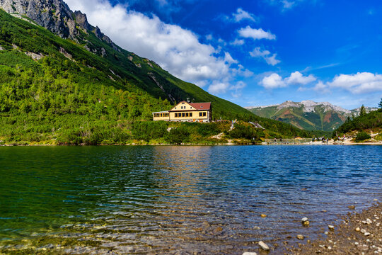 The famous wooden mountain cabin "Chata pri Zelenom plese" situated on the shore of a crystal clear alpine lake. Surrounded by steep mountain slopes and blue sky with white clouds in the Tatra Nationa