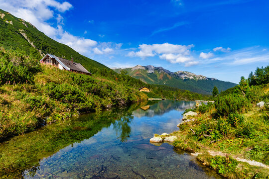 Transparent water of a mountain stream reflecting the blue sky. Captured in the High Tatras near Zelene pleso, with the scenic limestone ridge of Belianske Tatras in the distance and lush green vegeta
