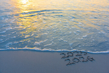 2025 written on the sand covered by a small wave while 2026 writing is untouched